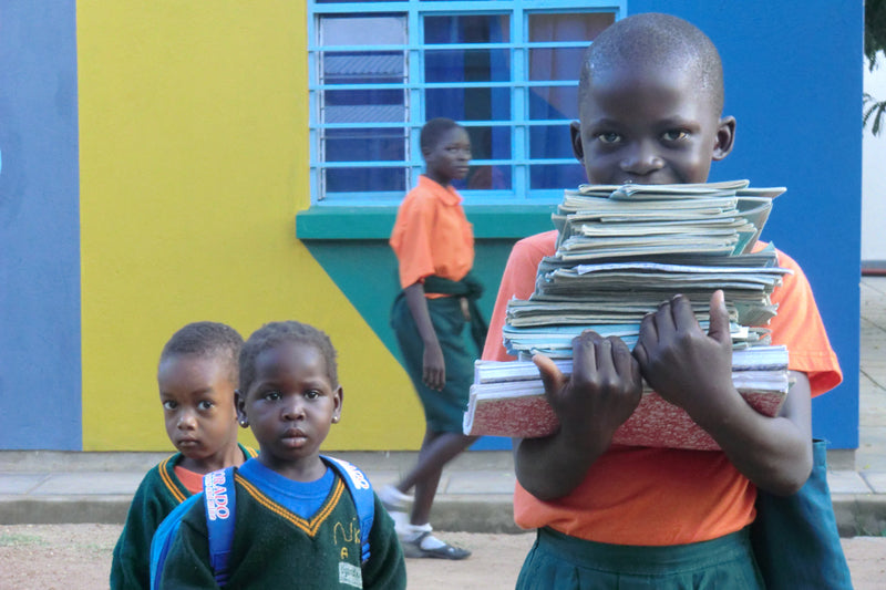 Kleine Kinder von Uganda Kids, eines Trägt Schulbücher